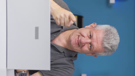 Vertical-video-of-Home-office-worker-man-makes-a-trust-sign-to-the-camera.